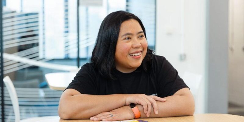 Photograph of Desi Pimarsari leaning on a table - smiling to someone off camera